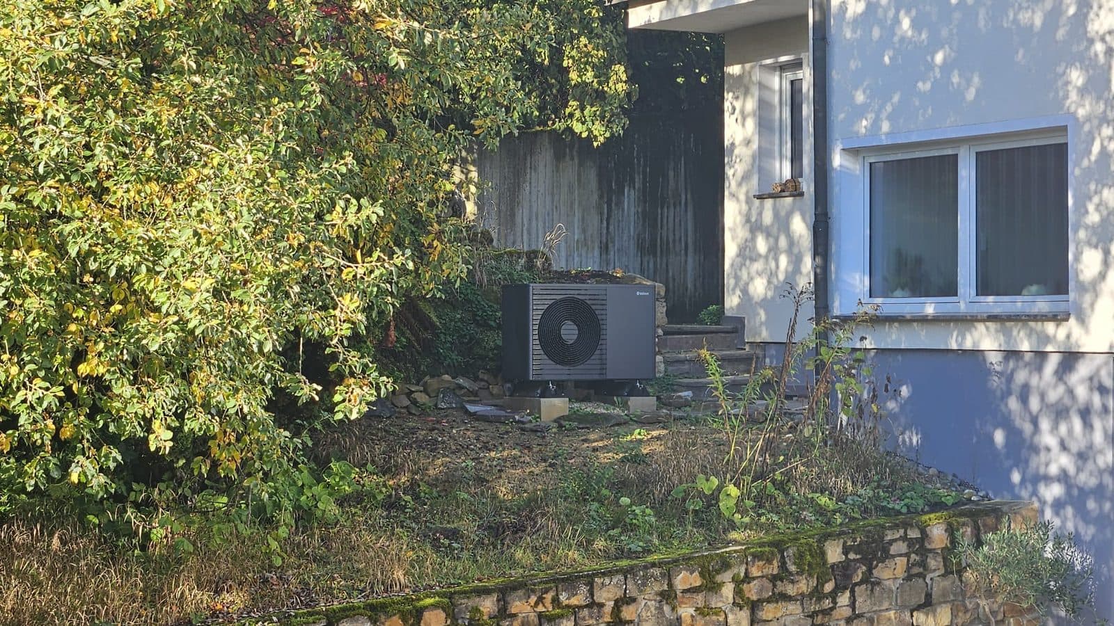 Luft-Wasser-Wärmepumpe im Garten eines älteren Einfamilienhauses